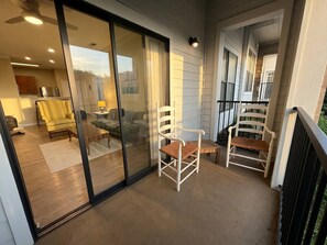 A modern interior with a glass door leading to a balcony, a yellow armchair, and a white chair with a wooden seat. - Modern Charlotte Apt - Pool, Gym, Game Room, & BBQ (Charlotte)