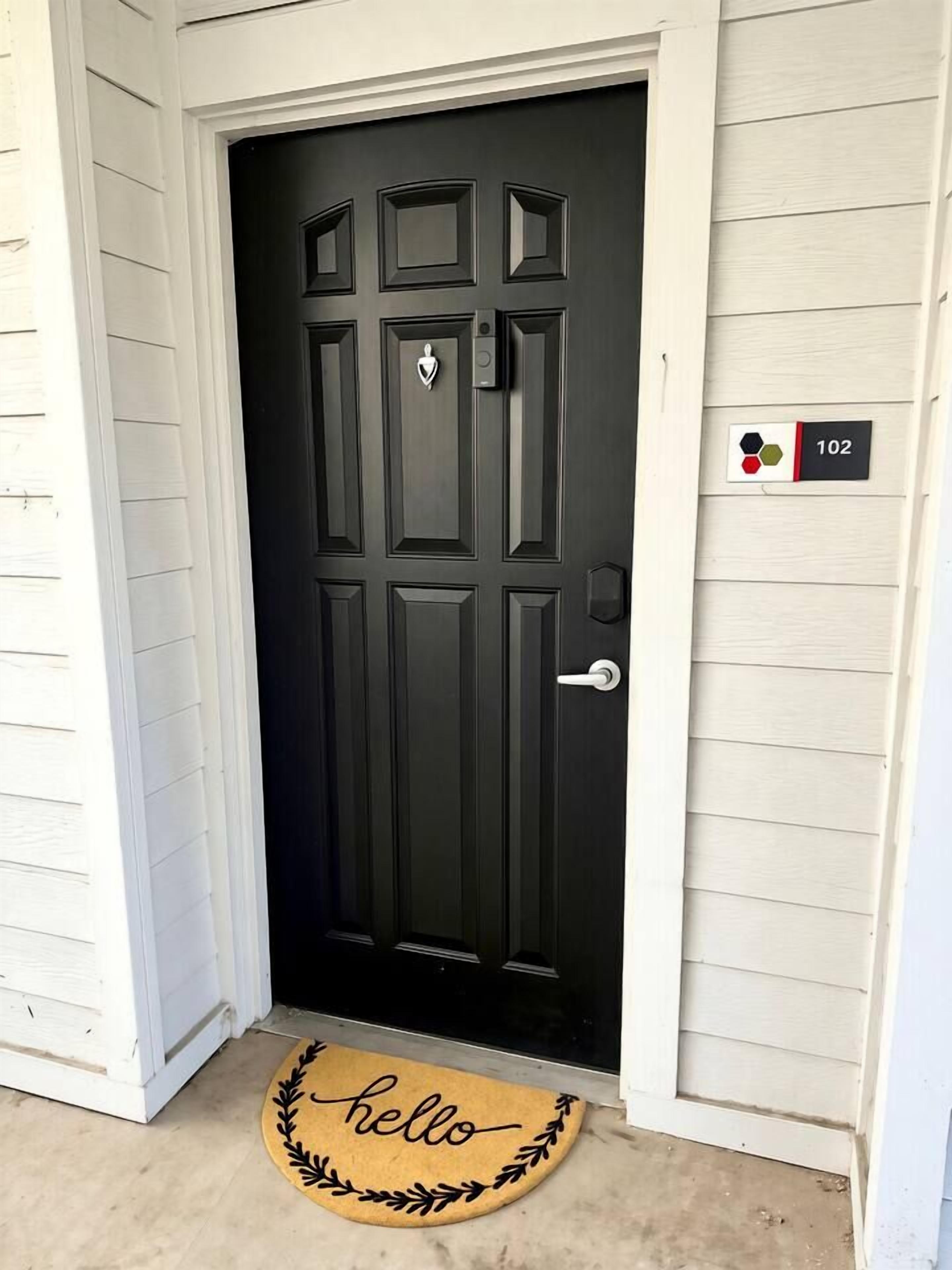 A black door with a doormat that reads 'hello' and a house number sign indicating '102'.