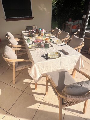 Ein Essbereich mit einem langen Tisch, der für eine Mahlzeit gedeckt ist, umgeben von mit Kissen ausgestatteten Stühlen.