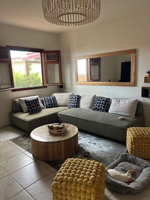 Ein modernes Wohnzimmer mit einem Ecksofa, einem runden Couchtisch und einem Körbchen für Haustiere.