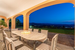 Eine Außenpatio mit einem runden Tisch und sechs Stühlen, umgeben von Bögen, mit Blick auf eine Wiese und sanfte Hügel in der Ferne.