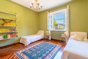 Ein Zimmer mit zwei Betten, einer Bücherwand, einem Chandelier und einem Fenster mit Blick.