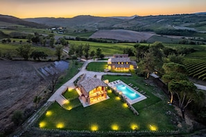 Eine Villa mit Schwimmbad, umgeben von üppiger Vegetation und Weinbergen, im Abendlicht.