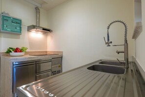 Eine kleine Küche mit Spüle aus Edelstahl, integriertem Backofen und Wandarmatur.