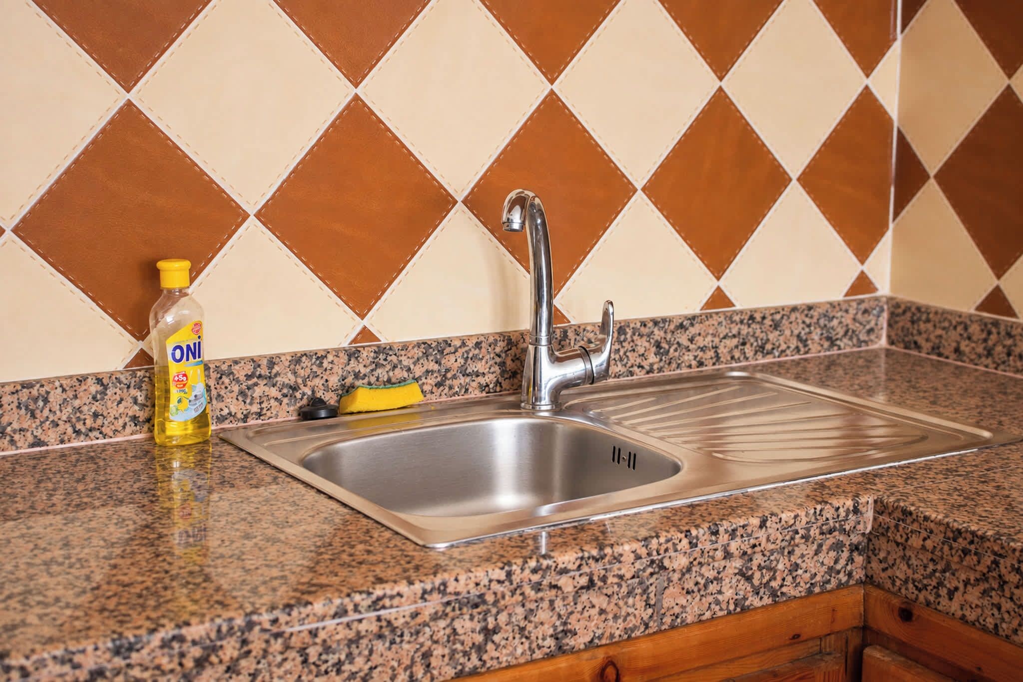 A kitchen with a stainless steel sink, granite countertop, and a bottle of dish soap.