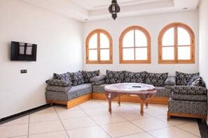 Une pièce comprenant un canapé d’angle, une table ronde et trois fenêtres en arc de cercle.