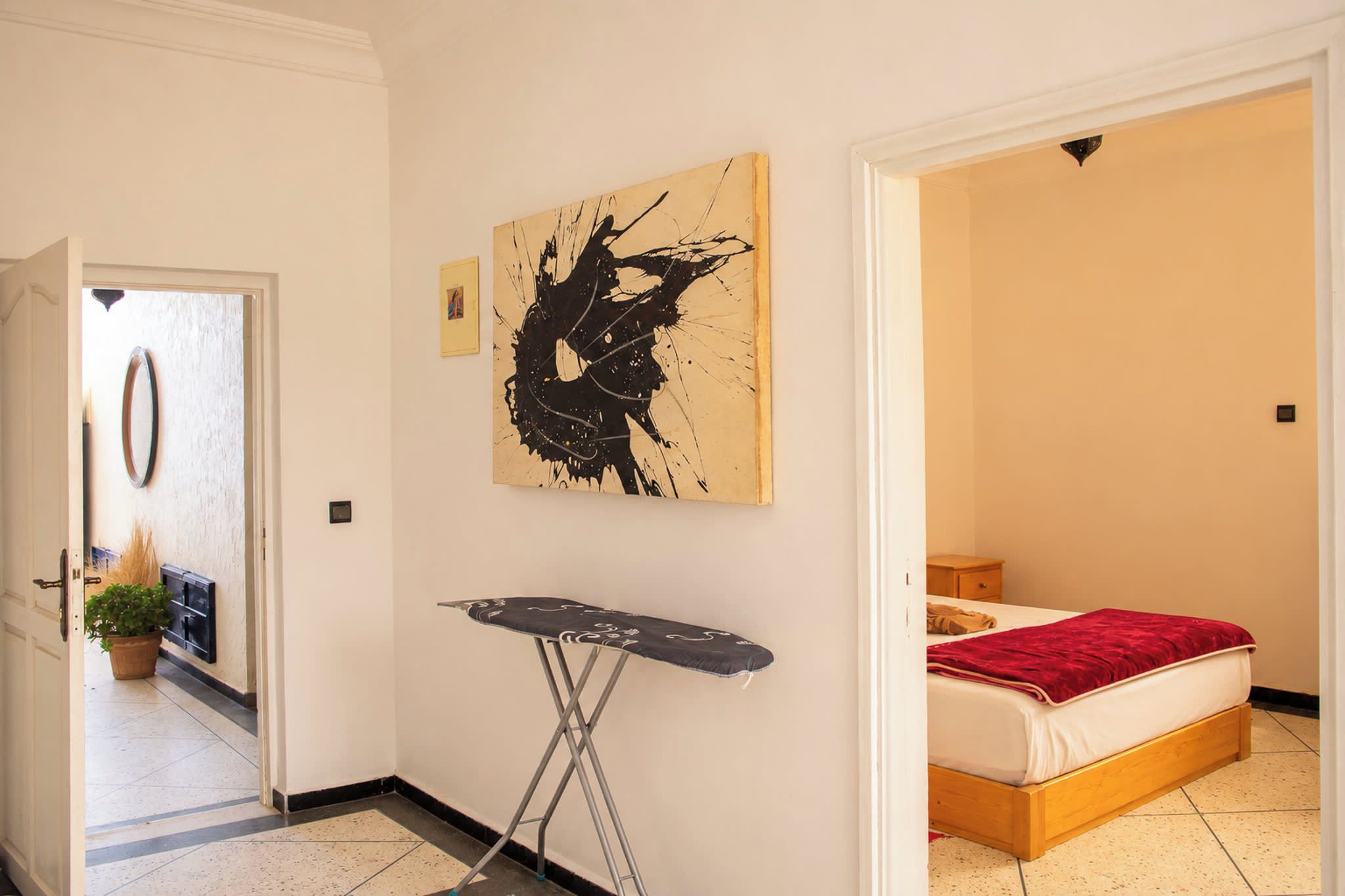 Ein Hotelzimmer mit einem Bett, einer roten Decke, einem Bügelbrett und einem Bild an der Wand.