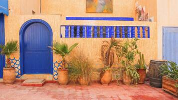 Un edificio con puerta azul, plantas en macetas y un barril de madera.