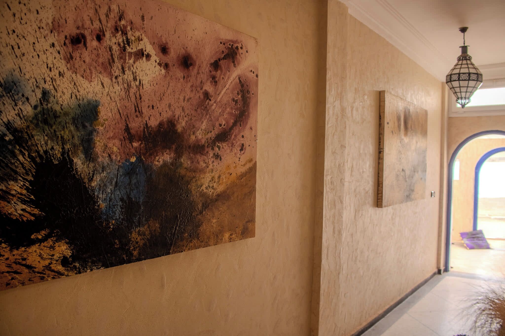 Un couloir avec une grande peinture abstraite sur le mur de gauche, un tableau encadré sur le mur de droite et une porte en arc de cercle au fond.