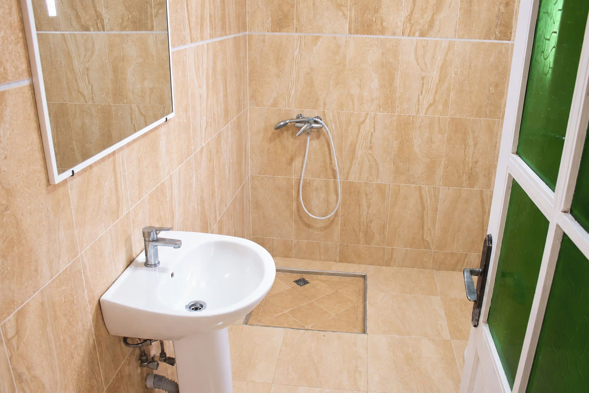 Une salle de bain avec un lavabo blanc, une douche équipée d’un pommeau de douche à main et une fenêtre à cadre vert.