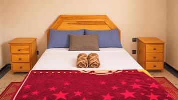 A hotel room with a bed, two nightstands, a red blanket with stars, and a wooden headboard.