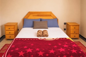 Une chambre d’hôtel avec un lit, deux tables de chevet, une couverture rouge ornée d’étoiles et une tête de lit en bois.