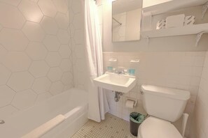 A bathroom with a hexagonal tile wall, a white sink, a toilet, and a shower curtain. - Expansive South End Studio (Boston)