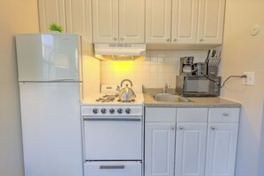 A compact kitchen with a refrigerator, stove, microwave, and a sink. - Expansive South End Studio (Boston)