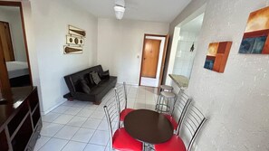 A room with a sofa, a dining table with chairs, and a door leading to another room. - Millenium Thermas Residence Condominium (Caldas Novas)