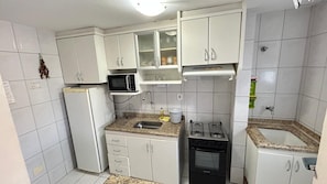 A compact kitchen with white cabinets, a microwave, a sink, a stove, and a refrigerator. - Millenium Thermas Residence Condominium (Caldas Novas)