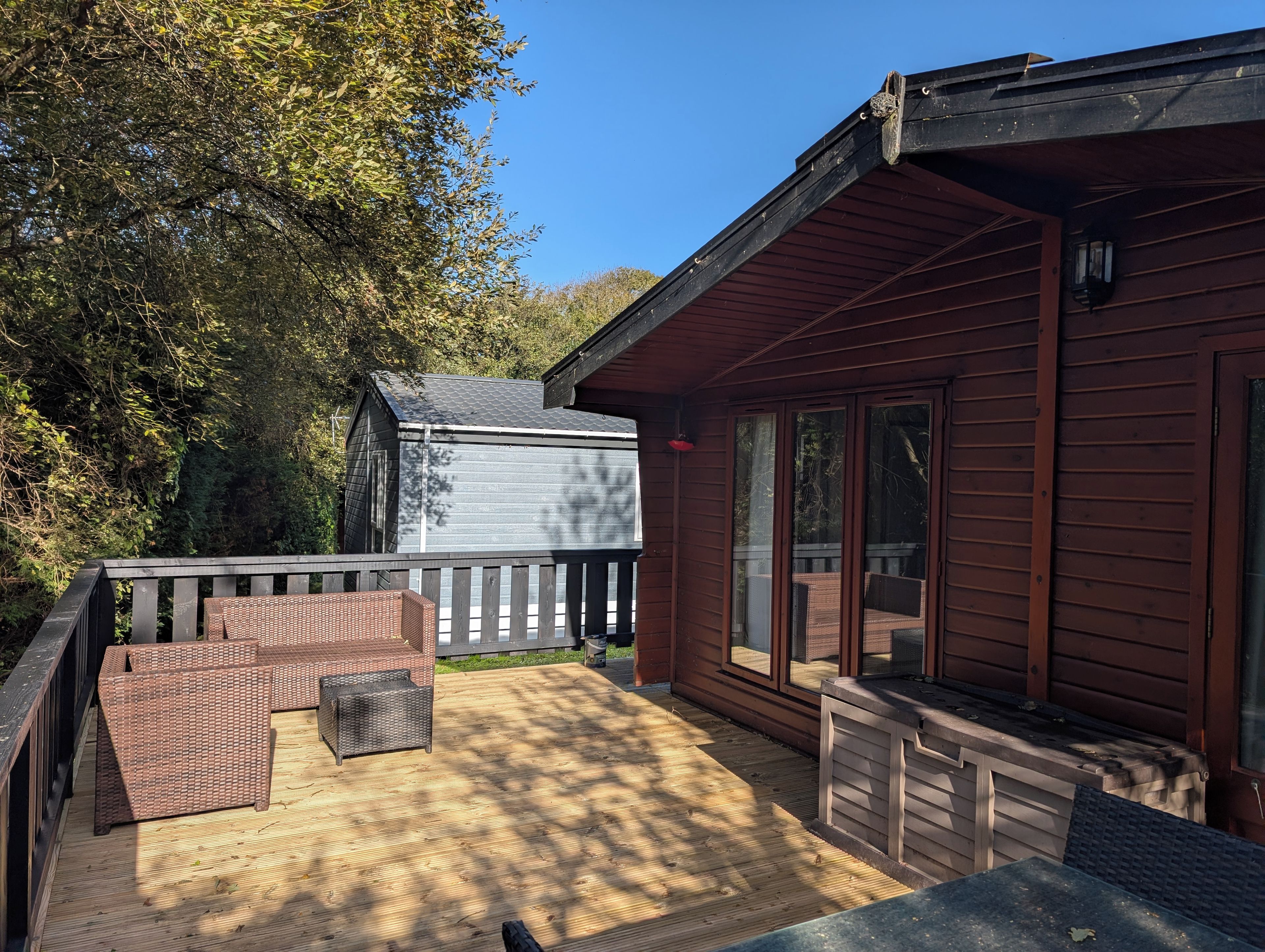 A wooden deck with wicker furniture, a small shed, and a house with large windows.