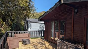 A wooden deck with wicker furniture, a small shed, and a house with large windows.
