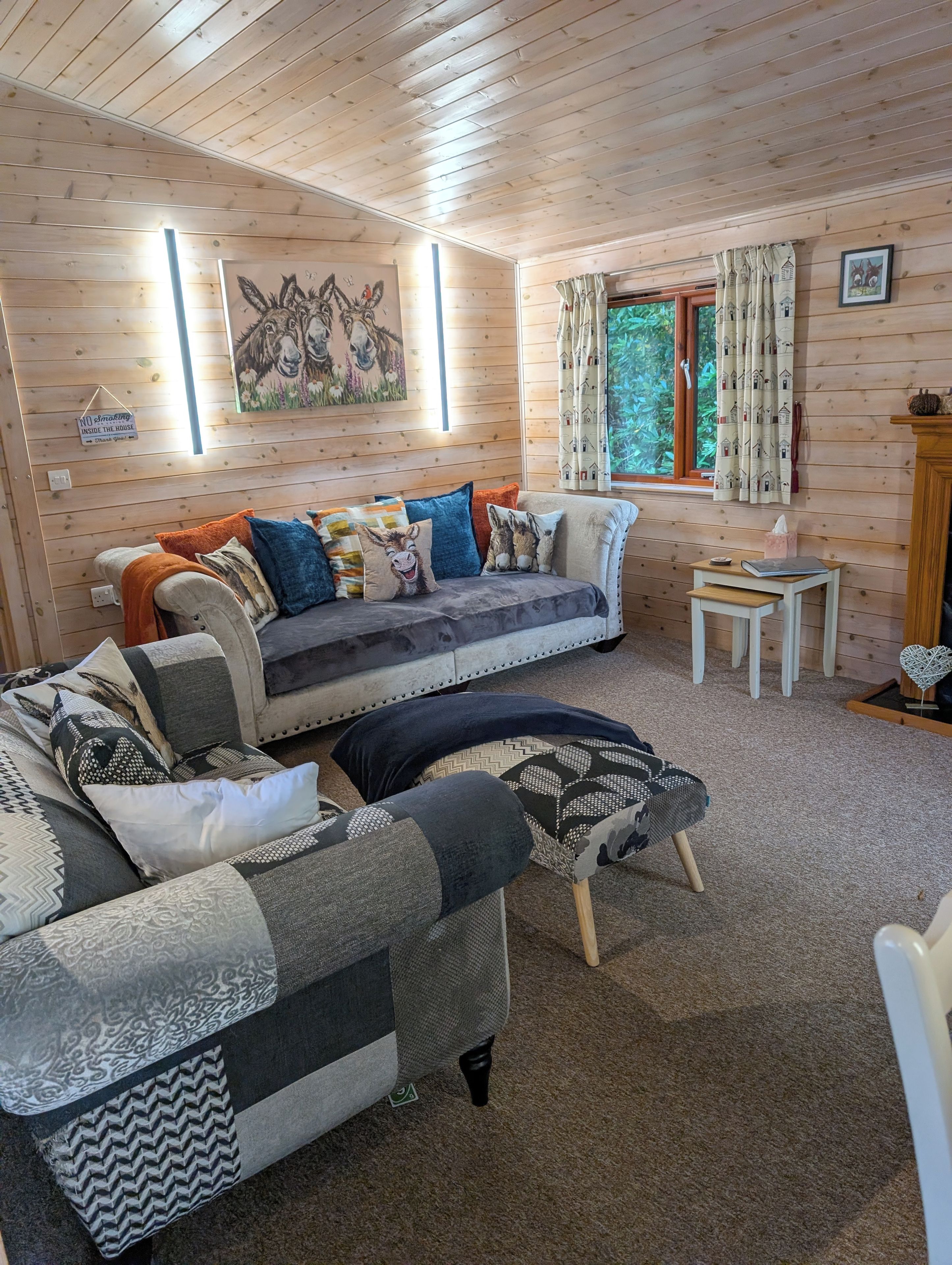 A cozy cabin interior with a sofa, a chair, a small table, and a window with curtains.