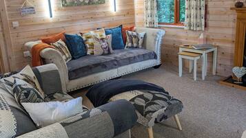 A cozy cabin interior with a sofa, a chair, a small table, and a window with curtains.