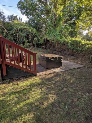 Een houten terras met rode leuning, een overdekte zithoek en een gazon.