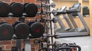 A gym with weightlifting equipment, including dumbbells and barbells, and a treadmill in the background.