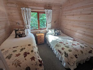 Een houten slaapkamer met twee bedden, een nachtkastje en een raam met gordijnen.