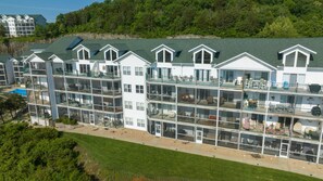 A multi-story hotel with balconies, a swimming pool, and a forested backdrop. - Lakefront Condo + Free Slip & Elevator access (Camdenton)