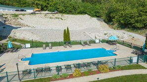 A rectangular swimming pool with a surrounding deck, a fenced area with lounge chairs, and a gravel path leading to a building. - Lakefront Condo + Free Slip & Elevator access (Camdenton)