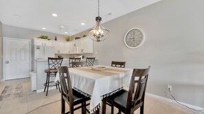 A dining area with a table set for four, surrounded by chairs, a chandelier, and a wall clock. - Lakefront Condo + Free Slip & Elevator access (Camdenton)