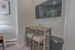A small room with a wooden table, two cushioned stools, a trash bin, and a mirror on the wall. - Spacious, Light-Filled Studio in the South End (Boston)