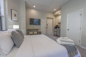 A hotel room with a bed, a desk, a chair, a TV, and a kitchenette. - Spacious, Light-Filled Studio in the South End (Boston)