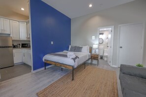 A bedroom with a bed, bedside table, and a bathroom visible through an open door. - Bold Studio Steps from Back Bay (Boston)