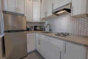 A modern kitchen with white cabinets, a stainless steel refrigerator, a microwave, and a gas stove. - Bold Studio Steps from Back Bay (Boston)