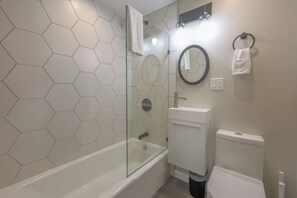 A bathroom with a glass-enclosed shower, a white sink, a toilet, and a mirror with a round frame. - Bold Studio Steps from Back Bay (Boston)
