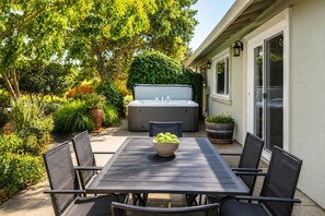 Eine Terrasse im Freien mit Tisch, Stühlen, einem Whirlpool und üppigem Grün.