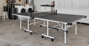 Ein tragbarer Tischtennis-Tisch auf Rädern in einem Raum mit Schränken im Industriedesign und einer Waschmaschine.