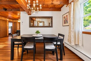 Ein Essbereich mit Holztisch, vier Stühlen, einer Chandelüster und einem großen Spiegel an der Wand.