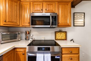 A kitchen with wooden cabinets, a microwave, a toaster, a stove, and a 'Welcome to the Poconos' sign. - Pocono Chalet Fireplace, Loft & Resort Fun (Lake Ariel)