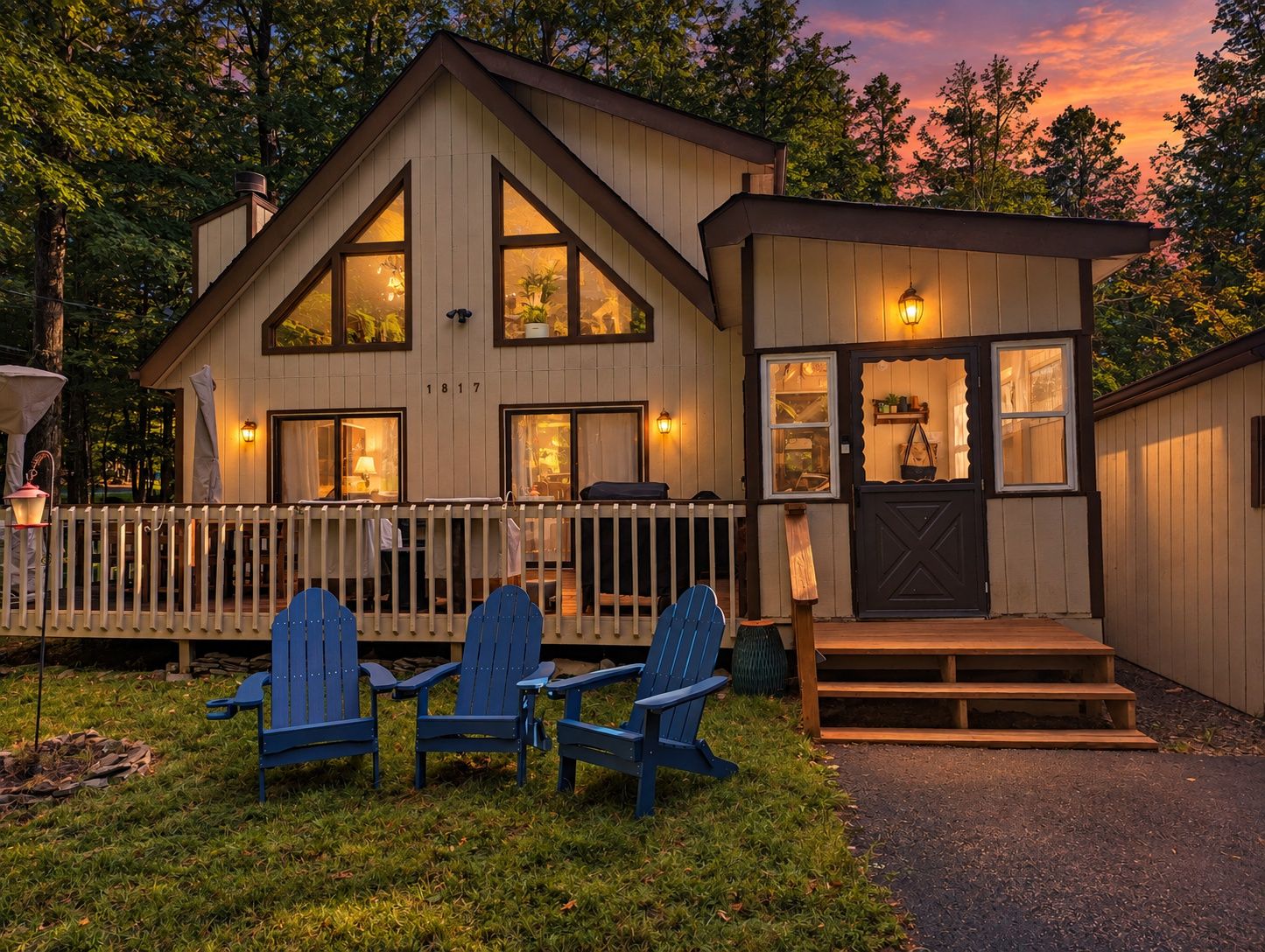 Ein zweistöckiges Holzhaus mit Veranda, blauen Adirondack-Stühlen und einer kleinen Terrasse.