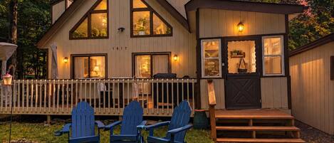 Ein zweistöckiges Holzhaus mit Veranda, blauen Adirondack-Stühlen und einer kleinen Terrasse.