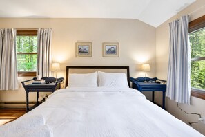 Ein Hotelzimmer mit einem großen Bett, zwei Nachttischen, einem Fenster mit Vorhängen und zwei gerahmten Bildern an der Wand.