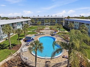 Ein Hotel mit einem zentral gelegenen Schwimmbad, umgeben von Palmen und Liegestühlen.