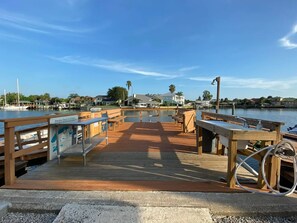 A wooden pier with benches and a signboard, overlooking a calm body of water with boats and houses in the background. - Great NSB Location on Intercoastal (New Smyrna Beach)