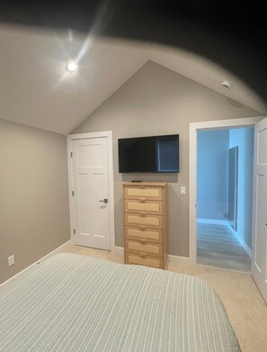 Ein Schlafzimmer mit schrägem Dach, einem Bett, einer Kommode und einem Fernseher.