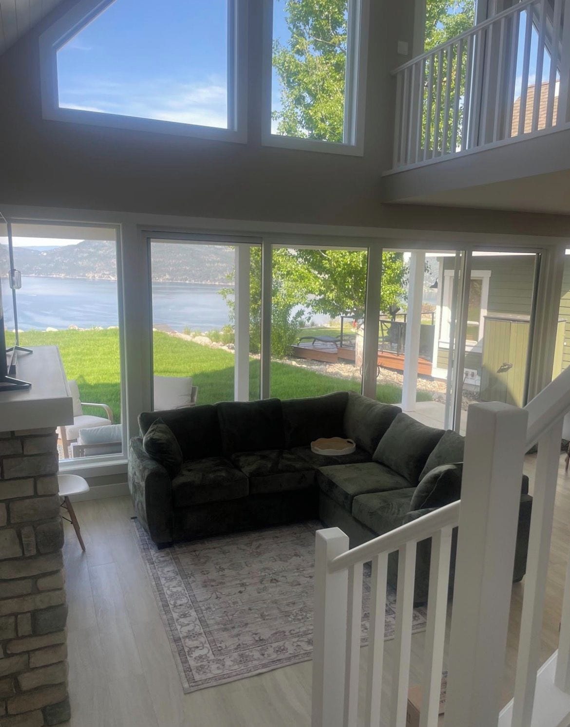 A spacious living room with a large sectional sofa, a stone accent wall, and a view of a lake through large windows.