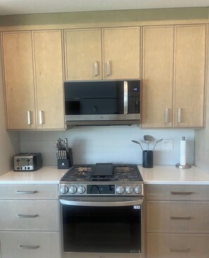 A kitchen with wooden cabinets, a microwave, a gas stove, and a toaster. - Cozy Okanagan escape between Big White & SilverStar - ski, relax & unwind! (Kelowna)