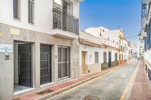 Uma rua estreita ladeada por edifícios, alguns com varandas e outros com acessos diretos.