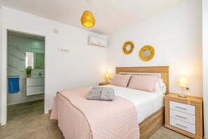 Quarto com cama, mesas de cabeceira, espelho e ar-condicionado fixado na parede.