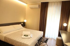 A hotel room with a bed, bedside lamps, an air conditioning unit, and a window with curtains.